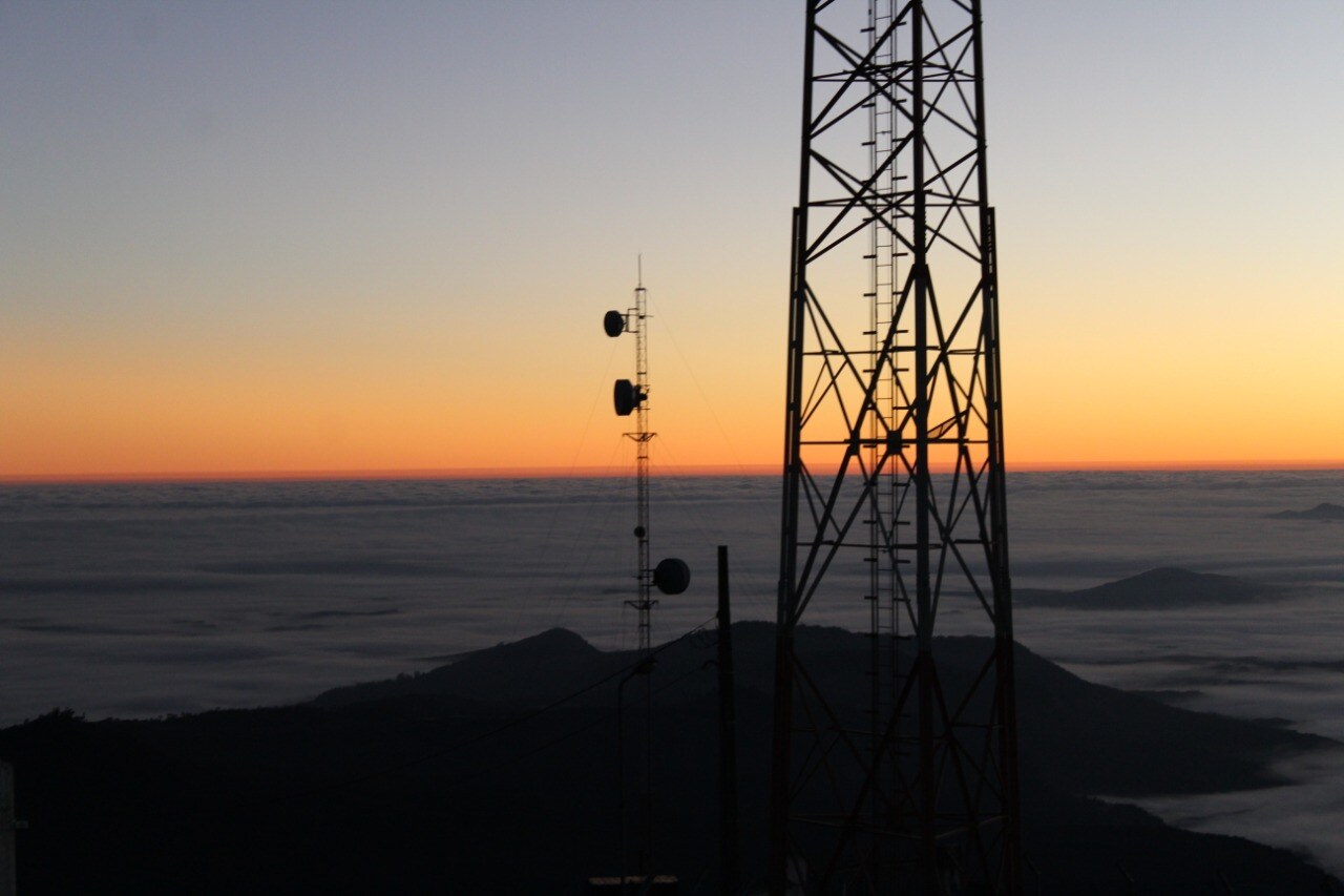 Antenas do Morro das Antenas silhuetadas contra o amanhecer, com mar de nuvens ao fundo
